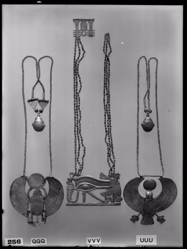 Image of negative of the back of three necklaces: the left one with a winged scarab, the middle one with a vulture, eye and cobra, and the right one with a falcon