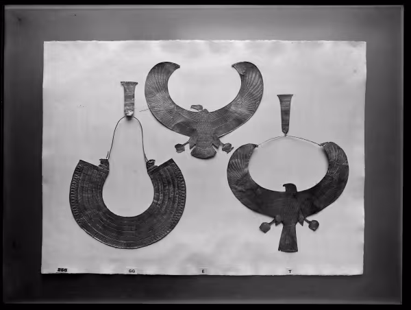 Image of negative of three collars: the left one of 'rainbow' shape with falcon head terminals, the middle one a vulture with outstretched wings, and the right one a falcon with outstretched wings