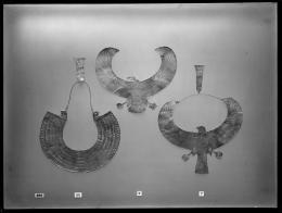 Image of negative of three collars: the left one of 'rainbow' shape with falcon head terminals, the middle one a vulture with outstretched wings, and the right one a falcon with outstretched wings